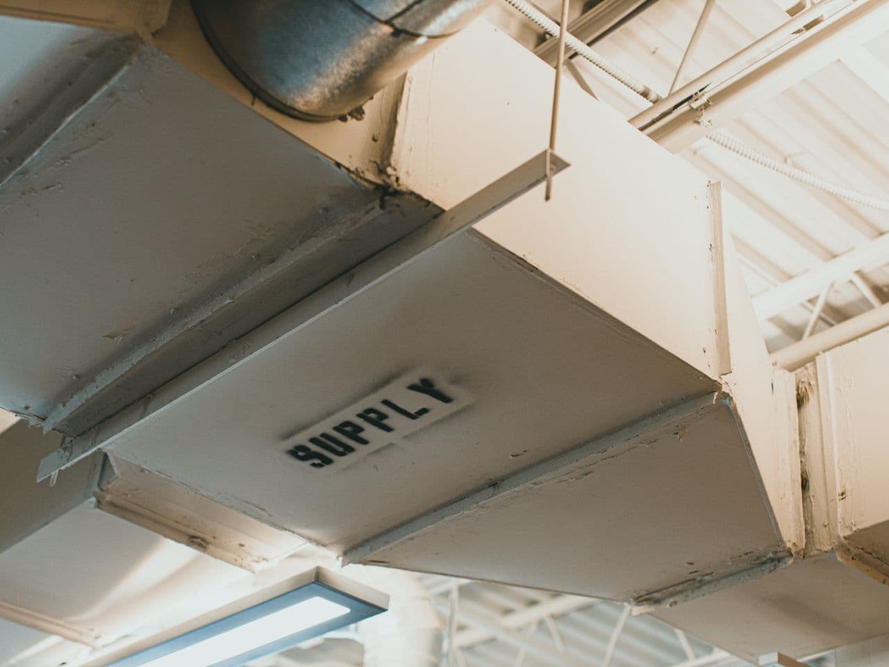 Cream-colored supply ducts installed along a mechanical room ceiling